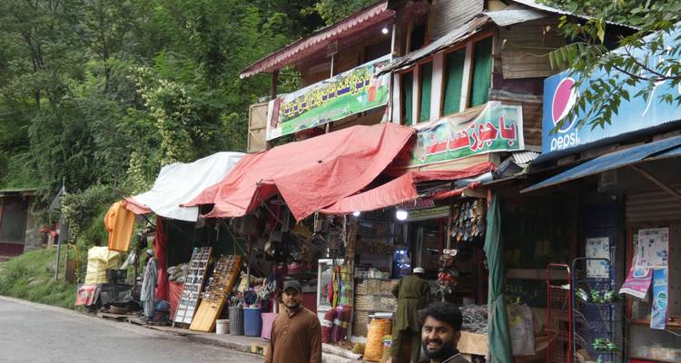 Small roadside bazaar with colourful awnings and local men standing in front of stalls in the hills.