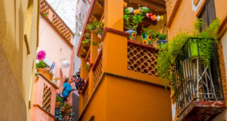 Kleurrijke smalle steeg met balkons versierd met bloemen en twee bezoekers die omhoog kijken.