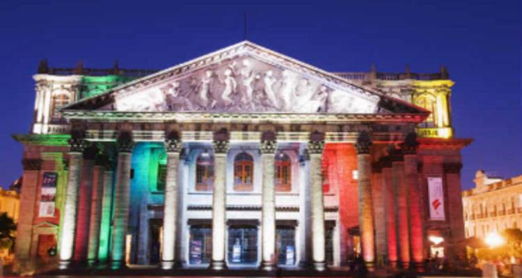 Neoklassieke theatergevel verlicht met rode, groene en witte lichten tegen een diepe nachtelijke hemel.