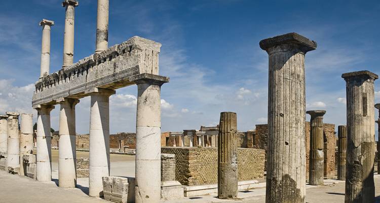 Antiguas columnas de piedra y ruinas de Pompeya que se alzan contra un cielo azul brillante.