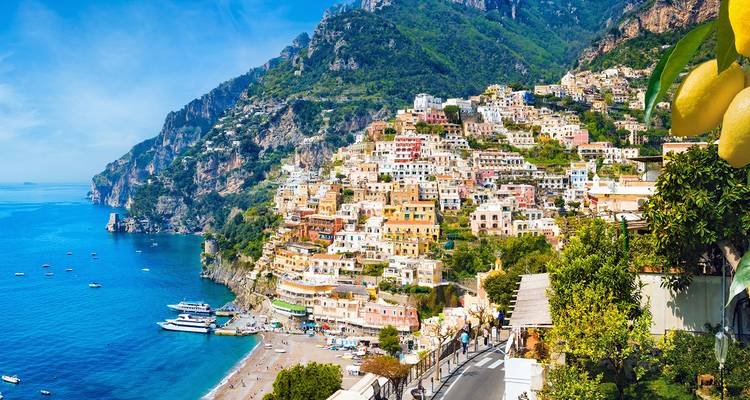 Casas coloridas en el acantilado de Positano que descienden en cascada hacia la turquesa Costa Amalfitana con barcos en la bahía.