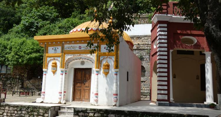 Small colorful Hindu temple building in lush hillside village setting.