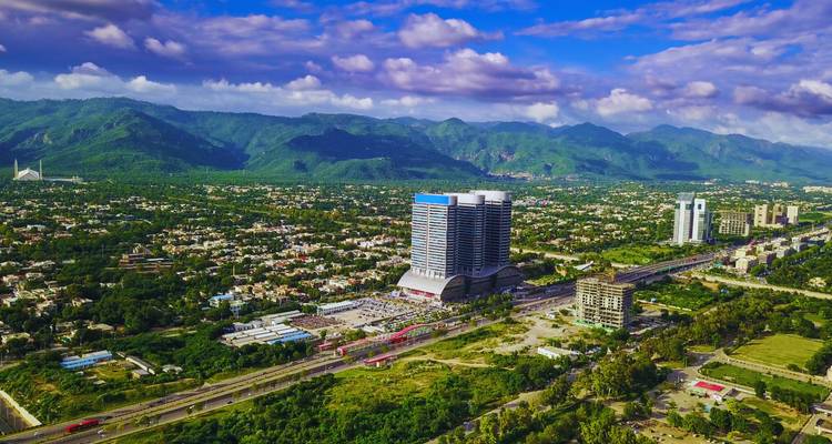 Wide aerial panorama of Islamabad city with mountains and scattered clouds in vivid daylight.
