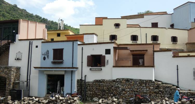 Row of pastel hillside houses with stone wall base and scattered motorbikes in foreground.