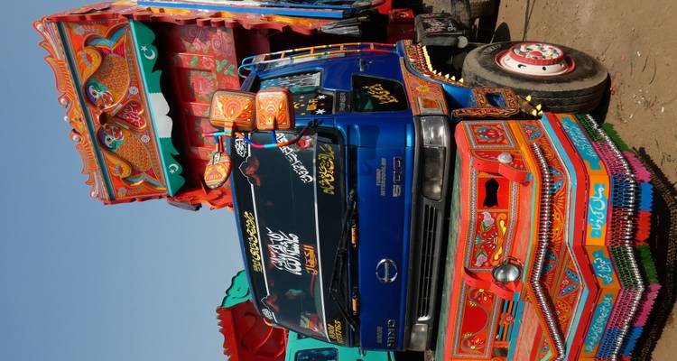 Vibrantly painted Pakistani truck covered in elaborate folk art parked on a dirt lot.