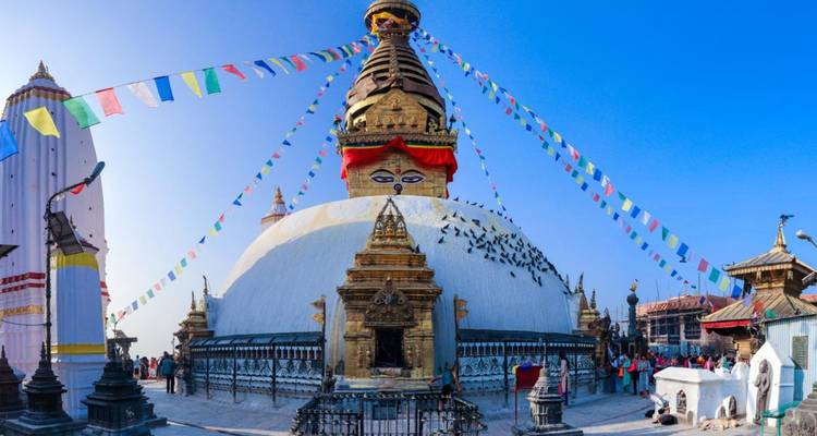 Die massive weiße Stupa von Boudhanath, behangen mit Gebetsfahnen unter einem leuchtend blauen Himalaya-Himmel.