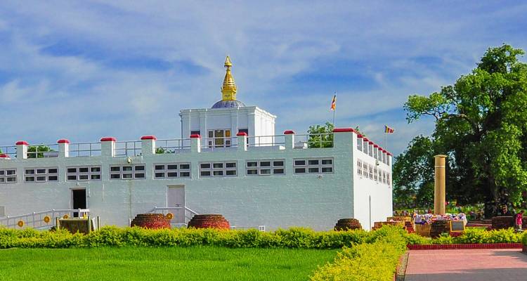 Der weiße Maya Devi Tempel in Lumbini, umgeben von gepflegten Rasenflächen, Gebetsfahnen und Pilgern.