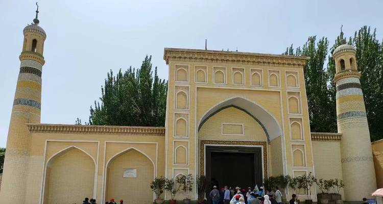 Besucher betreten die gelbe Backsteinmoschee Id Kah, die von Zwillingsminaretten und belaubten Pappeln flankiert wird.