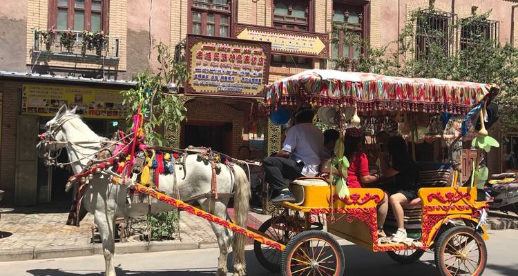 Eine von Pferden gezogene Kutsche, geschmückt mit bunten Stoffen, befördert Touristen durch die alten Straßen von Kashgar.
