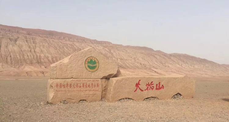 Ein gemeißeltes Steinmonument markiert den Fuß kahler, gestreifter Wüstenberge unter diesigem Licht.