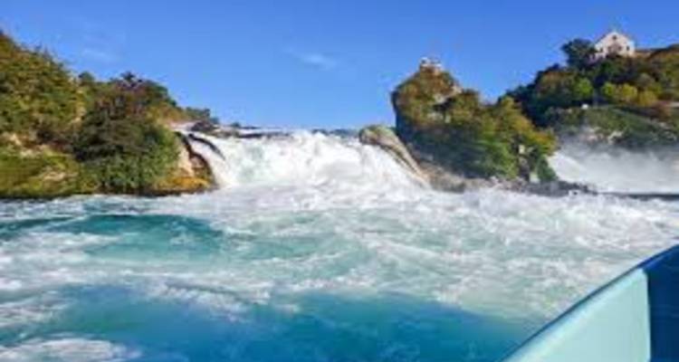 Mächtiger Wasserfall, der an einem sonnigen Tag in türkisfarbene Stromschnellen stürzt, betrachtet von einem Boot aus.