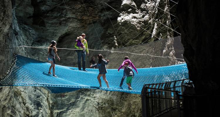 Avonturiers balanceren op een hangende blauwe netbrug in een dramatische rotskloof.
