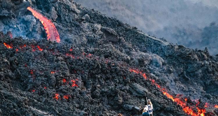 Un excursionista fotografía lava roja brillante fluyendo por una pendiente volcánica escarpada.