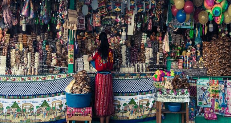 Una mujer vestida de manera tradicional acomoda pilas de dulces coloridos y juguetes en un puesto bullicioso del mercado.