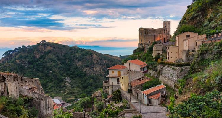 Village sicilien perché avec maisons en pierre et église surplombant des vallées luxuriantes au coucher de soleil coloré.