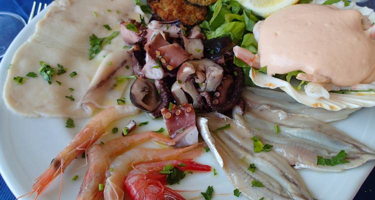 Plateau de fruits de mer avec crevettes, poulpe, filets de poisson et sauce servi dans une assiette blanche.