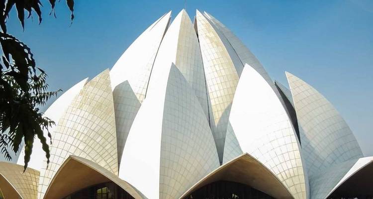 El Templo del Loto de pétalos blancos se alza contra un cielo despejado, enmarcado por ramas de árboles.