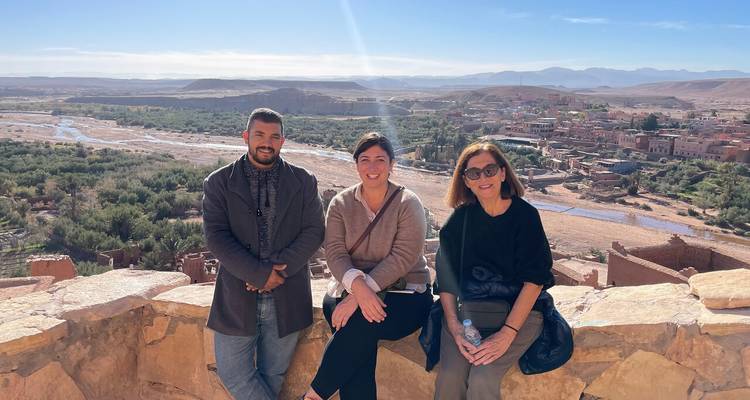 Kleine Gruppe posiert auf einer Steinmauer oberhalb eines üppigen Flusstals und Lehmziegeldorfs in der Nähe von Ait Benhaddou.