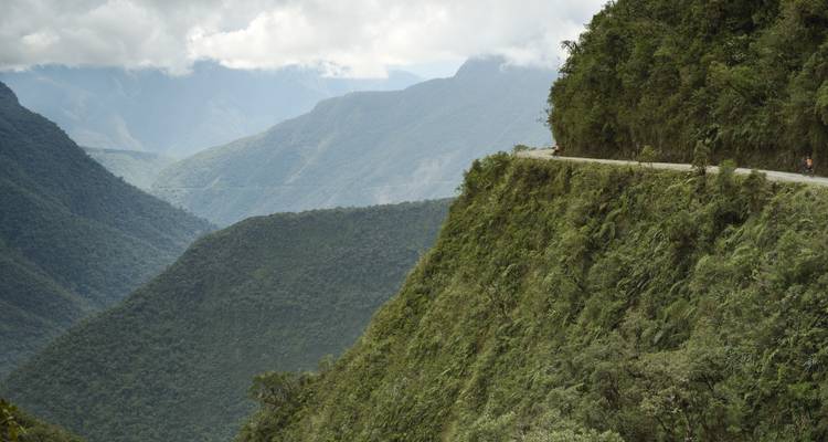 Route étroite longeant une falaise escarpée couverte de jungle au-dessus de vallées profondes et brumeuses.