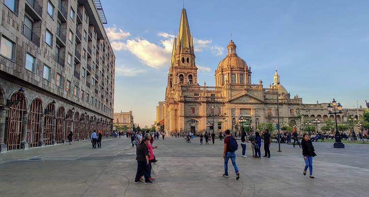 La lumière du soir baigne la cathédrale de Guadalajara tandis que les foules se promènent sur la vaste place de la ville.