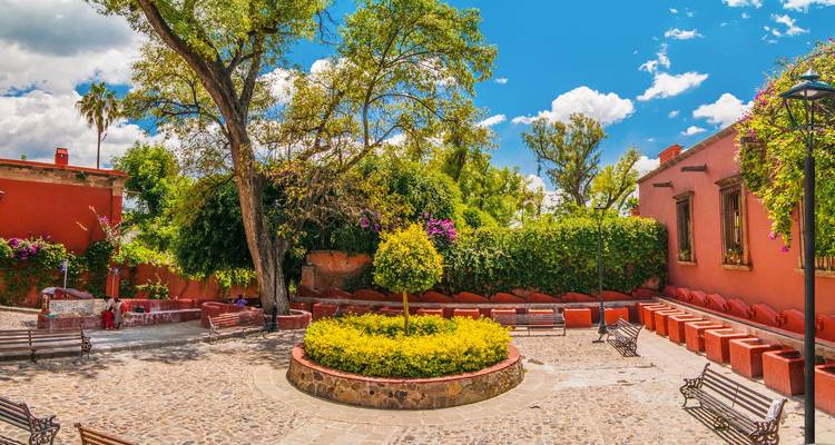 Cour colorée avec pavés, bancs, bougainvilliers en fleurs et murs éclatants sous un ciel bleu vif.