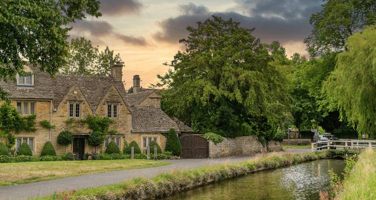 Cottage en pierre avec lierre et canal se trouve sous un ciel de coucher de soleil chaleureux dans les Cotswolds.