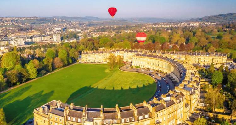 Vue aérienne du majestueux Royal Crescent de Bath avec des montgolfières au-dessus des pelouses vertes.