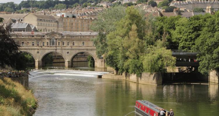 Le pont Pulteney en arche enjambe la rivière Avon avec un déversoir en cascade et des berges luxuriantes.
