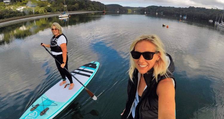 Deux femmes profitent du paddle sur une crique calme, souriant pour un selfie.