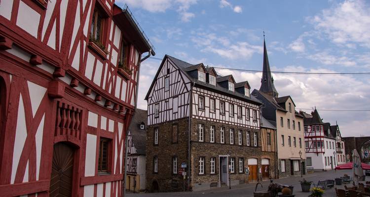 Traditionelle Fachwerkhäuser säumen eine ruhige Kopfsteinpflasterstraße unter einem teilweise bewölkten Himmel