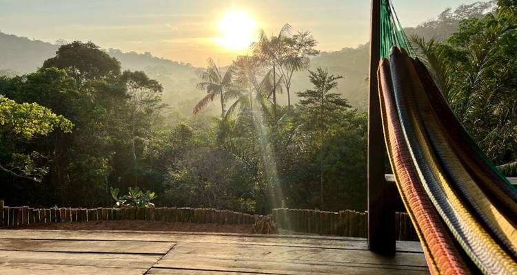 Sunrise view over lush Amazon jungle from a wooden deck with a colorful hammock in the foreground.