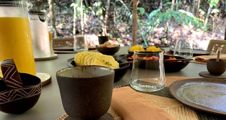 Outdoor breakfast table set with local food, juice and pottery surrounded by tropical forest.