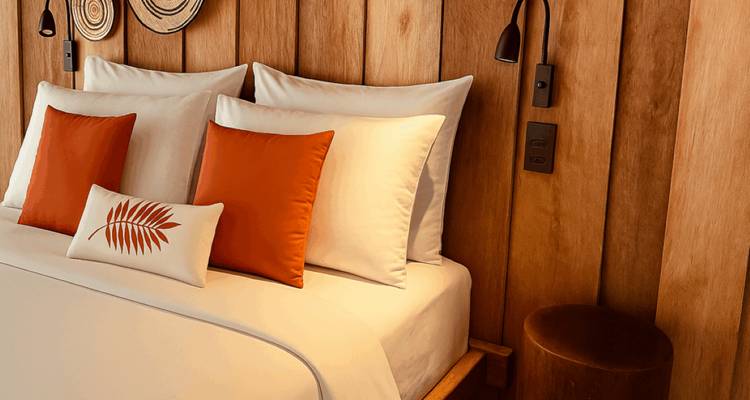 Stylish hotel bedroom with crisp white linens and orange accent pillows against wooden panel walls.
