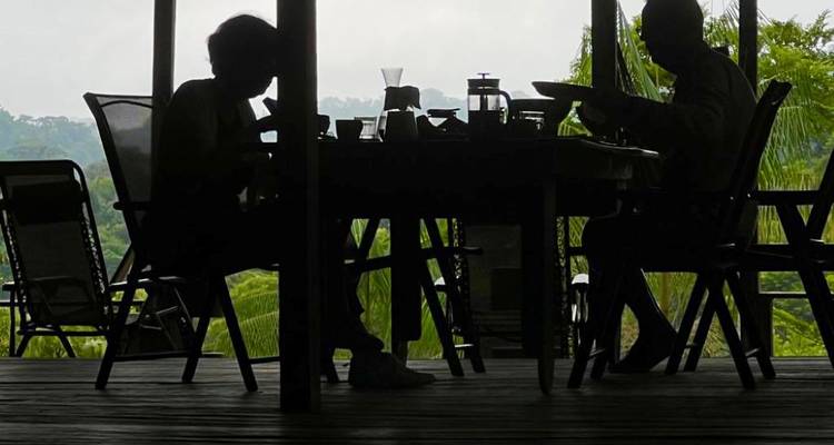 Silhouetted couple enjoying a meal on a covered terrace overlooking dense jungle.