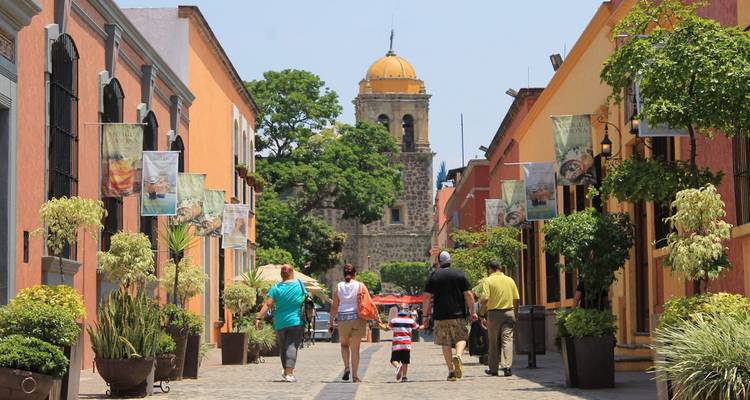 Rue piétonne coloniale colorée bordée de drapeaux et de plantes menant à un clocher d'église à dôme jaune.