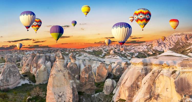 Lumière du coucher de soleil sur les vallées de roches roses de Cappadoce parsemées de montgolfières colorées.
