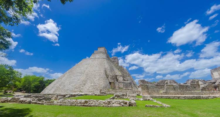 Steile Piramide van de Magiër in Uxmal onder levendige blauwe luchten met pluizige wolken.