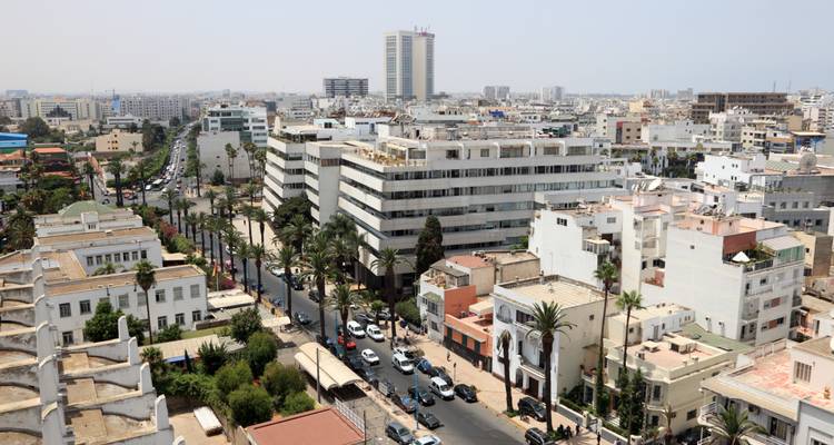 Panorama urbain moderne de Casablanca avec de larges avenues, des immeubles de taille moyenne et des gratte-ciel au loin par une journée brumeuse.