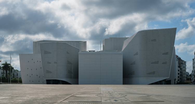 Ein modernes, kantiges, museumähnliches Gebäude in Casablanca steht vor einem dramatischen bewölkten Himmel auf einem leeren Platz.
