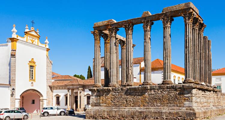 El templo romano bien conservado de Évora se alza imponente contra un cielo azul vívido junto a edificios encalados.