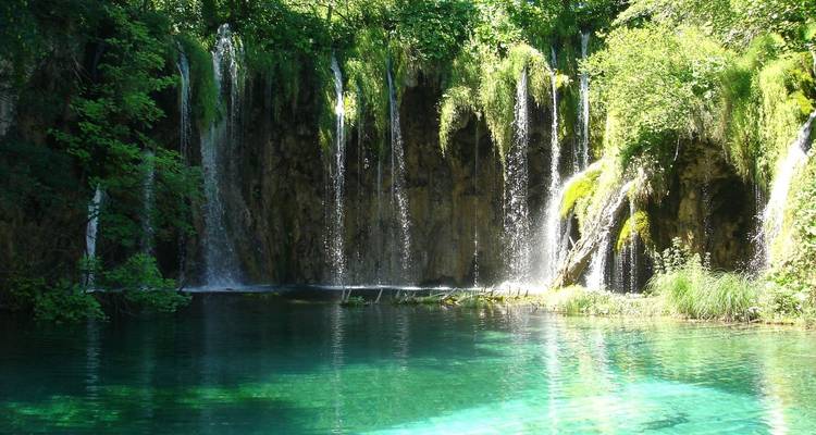 Kristalheldere turquoise poel gevoed door meerdere weelderig groene jungle watervallen in Plitvice Meren.