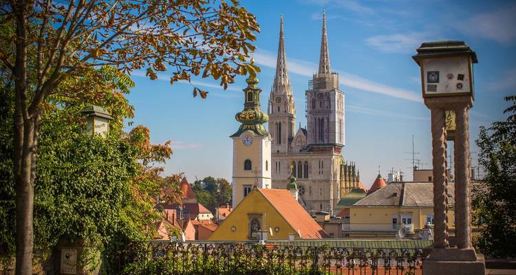 Charmant stadsgezicht met barokke kerkklokketoren en torens van de kathedraal van Zagreb omlijst door herfstbladeren.