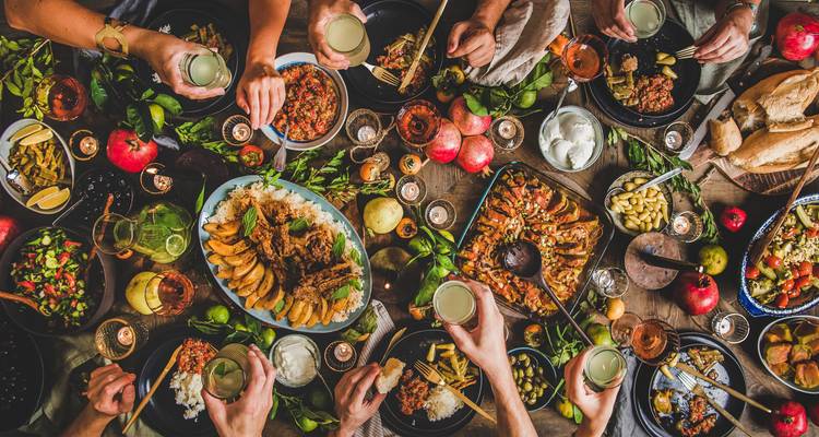 Übersicht-Festtafel beladen mit georgischen Gerichten, Früchten, Kerzen und mehreren Händen, die mit Gläsern anstoßen.