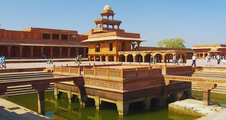 Roter Sandstein-Pavillon und Innenhof von Fatehpur Sikri mit Besuchern, die um ein grünes Wasserbecken spazieren.