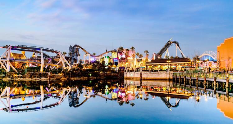 Las coloridas montañas rusas y atracciones de un parque temático se reflejan perfectamente en una laguna tranquila al anochecer.