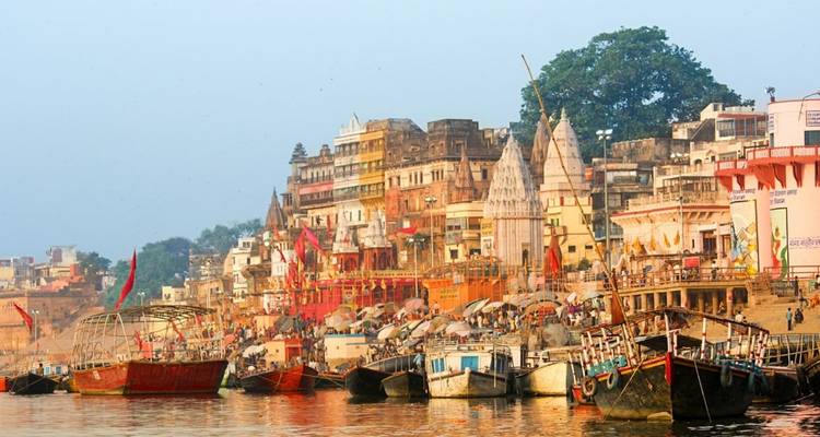 Farbenfrohe Ghats und Tempel entlang des Ganges in Varanasi mit Booten, die am Wasser vor Anker liegen.