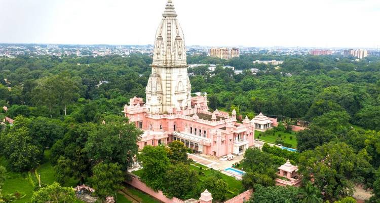Ein rosa getönter hinduistischer Tempelkomplex, umgeben von dichtem Grün und Stadtlandschaft in der Ferne.