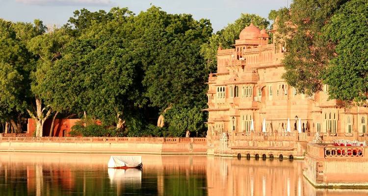 Eleganter Palast am Seeufer aus rosa Sandstein, der sich in stillem Wasser spiegelt, umgeben von üppig grünen Bäumen.