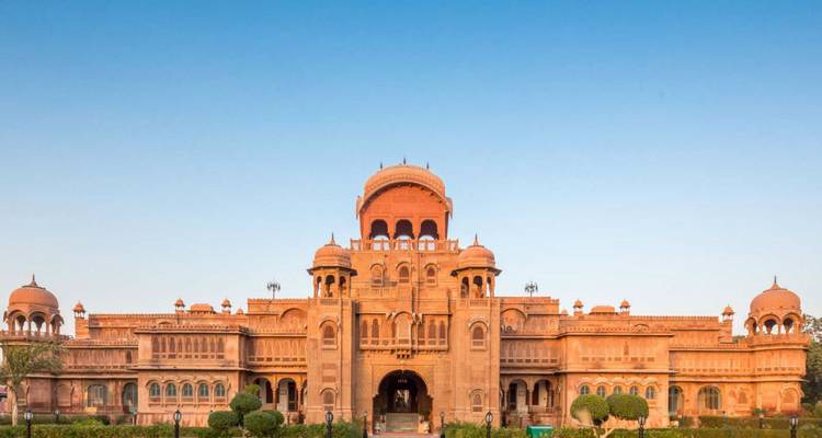 Symmetrischer roter Sandsteinpalast mit mehreren Kuppeln vor einem klaren blauen Himmel.