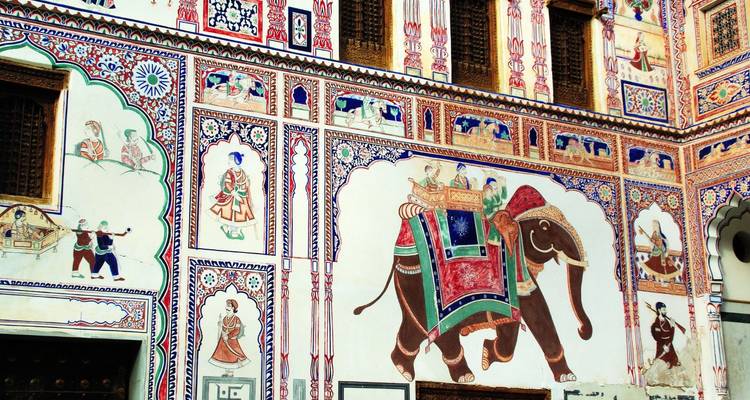 Farbenfrohe Fresken, die Elefanten und königliche Szenen darstellen, schmücken die Wände eines traditionellen Havelis.